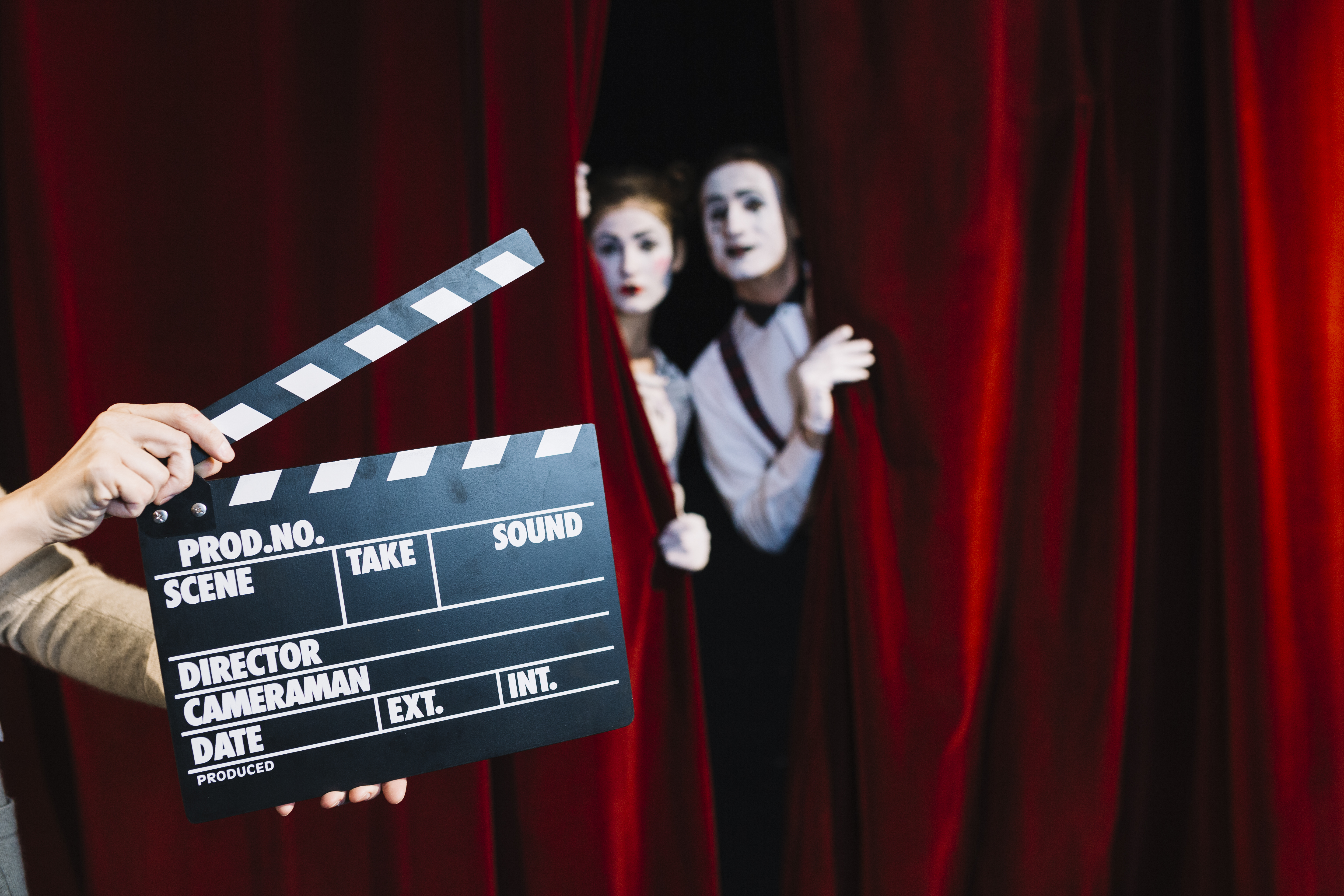person-holding-clapperboard-front-mime-couple-standing-red-curtain
